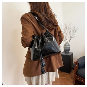 Détail d'un sac seau en cuir ciré noir avec cordon de serrage et pompon décoratif