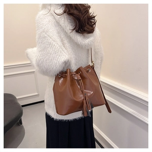 Détail d'un sac seau en cuir marron brillant avec glands à franges et fermeture à cordon