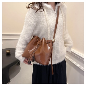 Détail du sac seau marron vintage avec cordon de serrage, pompons et texture cuir brillant