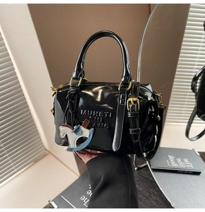 Detail of black patent leather Boston bag featuring embossed letters and a blue horse charm