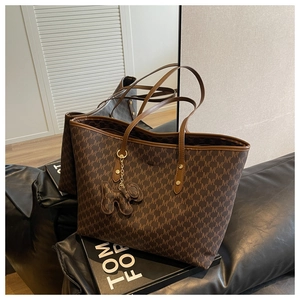 Detail of dark brown monogram tote bag with leather straps and a bear charm accessory