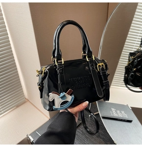 Detail of glossy patent leather mini bag with embossed letters and a toy horse charm