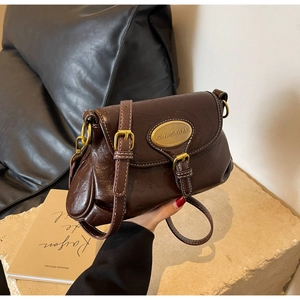 Detail of vintage brown oil-wax leather shoulder bag with metallic buckle and oval nameplate