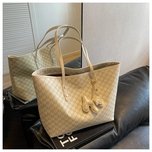 Detail of beige tote bag with M-pattern print and dog charm on a leather sofa