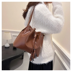 Détail du sac seau marron foncé brillant avec cordon de serrage et pompon sur blanc