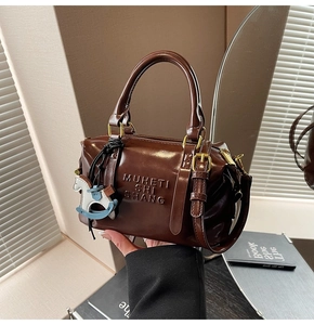 Close-up of dark brown leather pillow bag with embossed logo and metal zipper detail