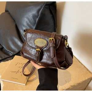 Detailed view of dark brown vintage shoulder bag with textured leather and gold oval plaque