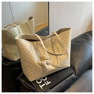 Detail of cream monogram tote bag with bear charm and long straps in a mirrored setting