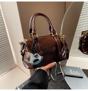 Detail of Boston bag in dark brown patent leather with horse charm and golden hardware