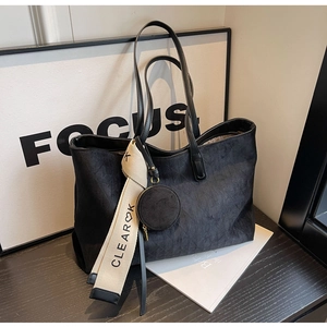 Detail of black leather tote bag with a wide beige logo strap and round charm pouch