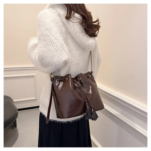 Détail d'un sac seau vintage marron foncé avec cordon de serrage, pompon et cuir brillant