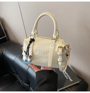 Close-up of cream Boston bag with embossed text detail and a blue horse charm