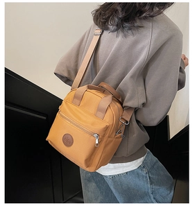Detail of a ginger yellow nylon crossbody bag with side pocket and brown leather logo