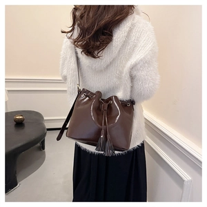 Détail d'un sac seau marron à cordon avec glands porté par un mannequin en intérieur chic