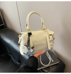 Detailed view of white leather boston bag with embossed letters and a horse charm