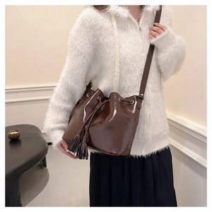Sac seau marron foncé avec franges et détails dorés porté par un mannequin chic