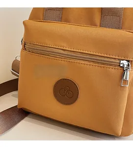 Detail of ginger yellow crossbody bag with zipper pocket and round leather logo patch