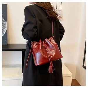 Détail d'un sac seau en cuir verni bordeaux avec cordon de serrage, pompons et œillets dorés