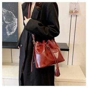 Détail du sac seau bordeaux à cordon avec texture cuir brillant et pompons décoratifs