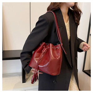 Détail du sac seau bordeaux à cordon avec pompons à franges et finition brillante