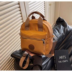 Detail of a ginger yellow nylon crossbody bag featuring double handles and a round leather logo