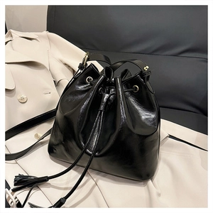 Détail du sac seau noir en cuir brillant avec fermeture à cordon et pompons élégants