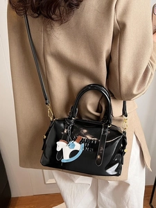 Chic black patent leather Boston bag with embossed letters and charm on a stylish model