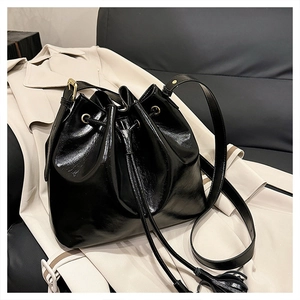 Détail d'un sac seau noir brillant à cordon avec ferrures dorées sur manteau