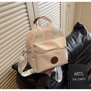 Detail of off-white nylon crossbody bag showing the front zip pocket and brown logo patch