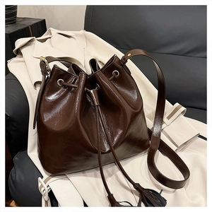 Détail du sac seau plissé marron foncé brillant avec cordon à gland et boucles dorées