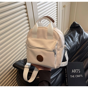 Detail of a beige nylon crossbody bag with brown leather handles on a black sofa