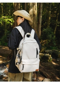 Detailed view of the large ivory outdoor backpack with leather logo in a forest setting