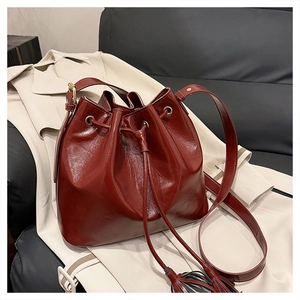 Détail du sac seau bordeaux avec cordon de serrage, pompons et cuir verni brillant