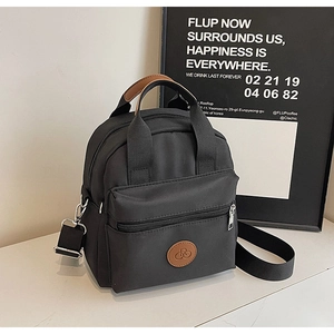 Detail of black mini crossbody bag featuring dual zippers and front pocket with leather patch