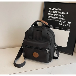Close-up of black nylon crossbody bag with brown leather logo and silver zipper details