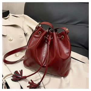 Gros plan du sac seau bordeaux avec pompons et détails dorés sur un manteau