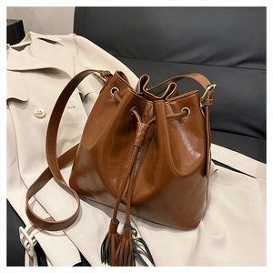 Détail du sac seau marron foncé avec fermeture à cordon et pompons élégants en cuir synthétique