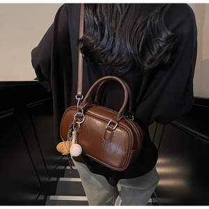 Détail d'un sac oreiller rétro marron foncé avec texture et breloque baseball sur modèle
