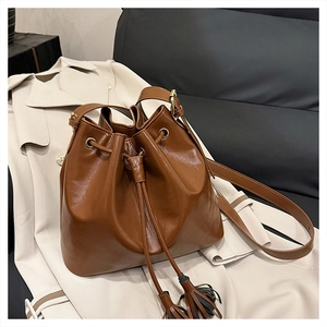 Détail d'un sac seau marron foncé avec texture plissée, cordon de serrage et longs glands