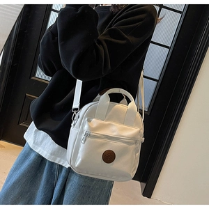 Detail of a white nylon crossbody bag featuring a circular logo and adjustable strap