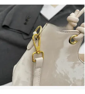 Detailed close-up of premium gold hardware and glossy cream leather on woman's bucket bag