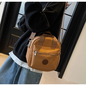 Detailed view of a brown nylon crossbody bag with front zipper and round logo patch