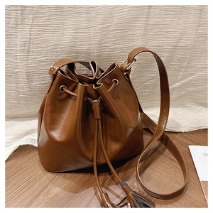 Détail du sac seau en cuir marron avec fermeture à cordon et pompons décoratifs