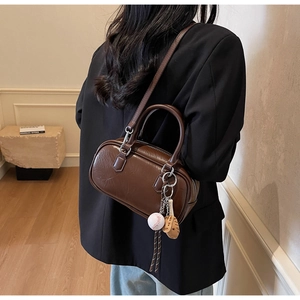 Détail d'un sac Boston vintage marron foncé avec breloques baseball et finitions argentées
