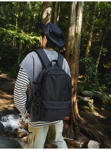 Detailed close-up of a large black nylon backpack with a brown leather logo in a forest