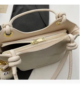 Detail view of a smooth metal zipper and knotted handle on a beige tote bag with a plush charm