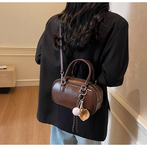Détail d'un sac polochon plissé marron avec doubles poignées et breloque baseball
