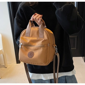 Detail of a brown nylon crossbody bag featuring a front zipper pocket and round logo
