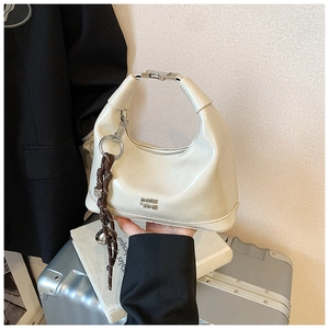 Detail of a beige patent leather crescent bag with metal buckle and woven charm