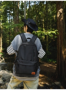 Outdoor shot of the black minimalist backpack with a brown leather logo and padded straps